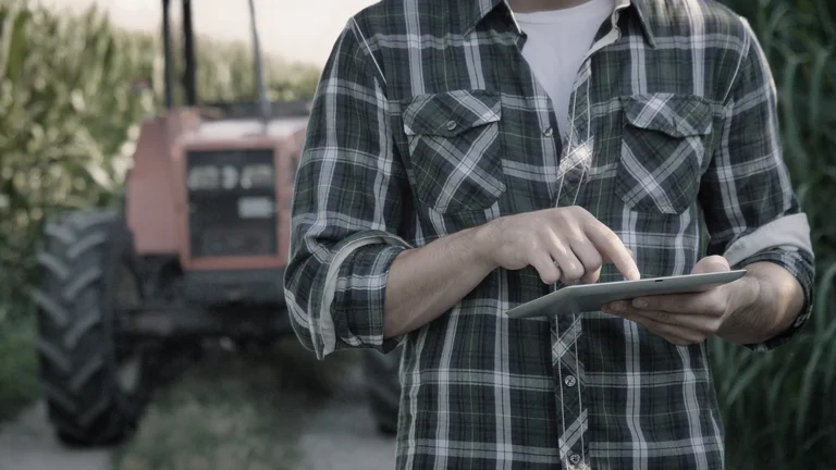 Portrait of a beautiful young farmer (student) working in the field with a tractor working in a tablet, happy, in a shirt, corn field. Concept ecology, transport, farmers, clean air, food, bio product